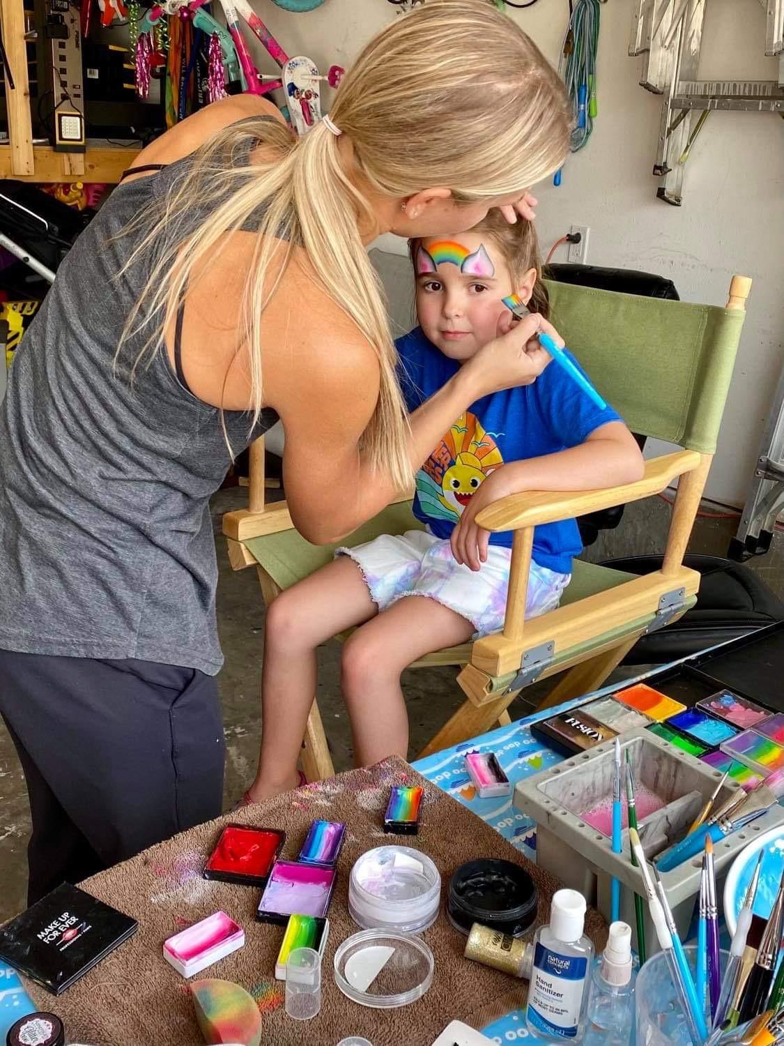 Sofya applying a colorful rainbow design on a young boy's forehead