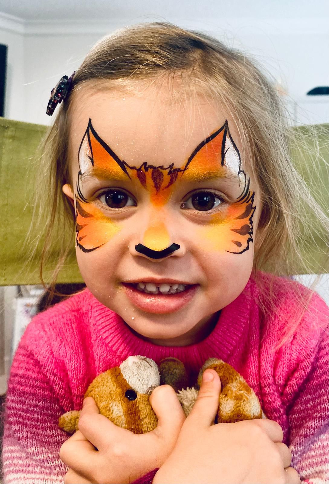 A young girl with an orange fox face painting