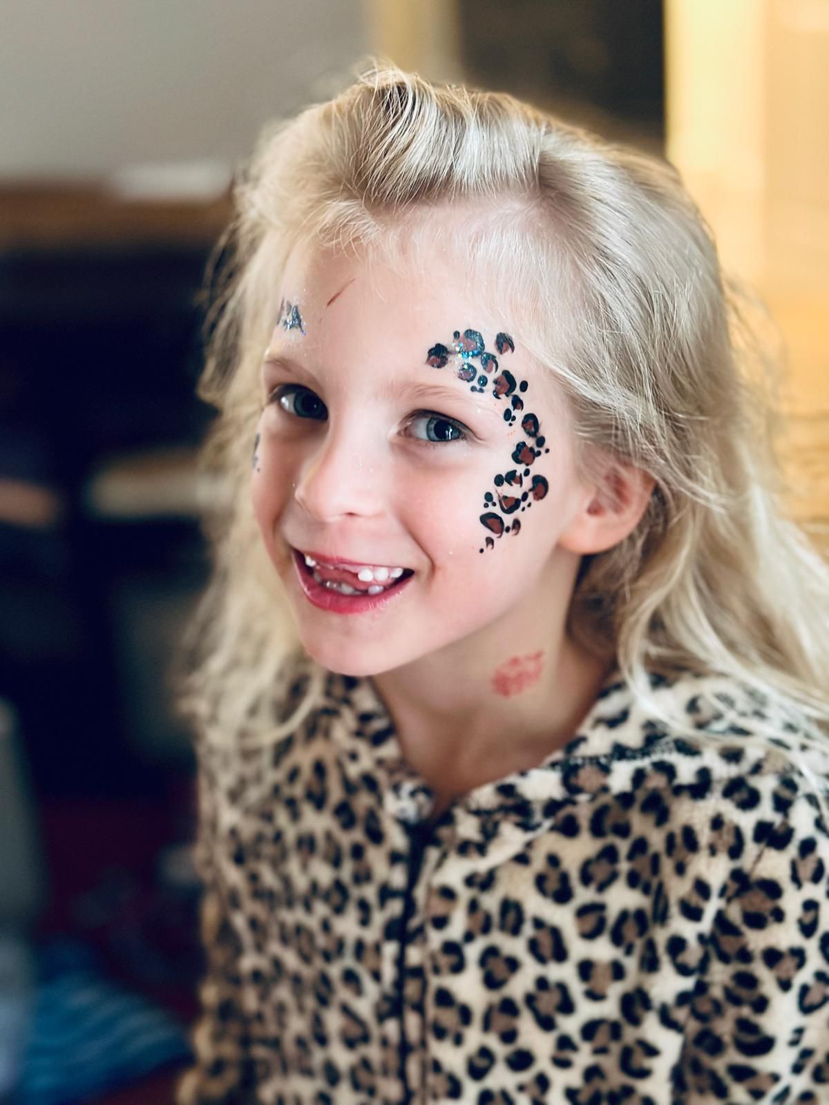 A smiling girl in a leopard-print outfit with a sparkling floral design on her cheek