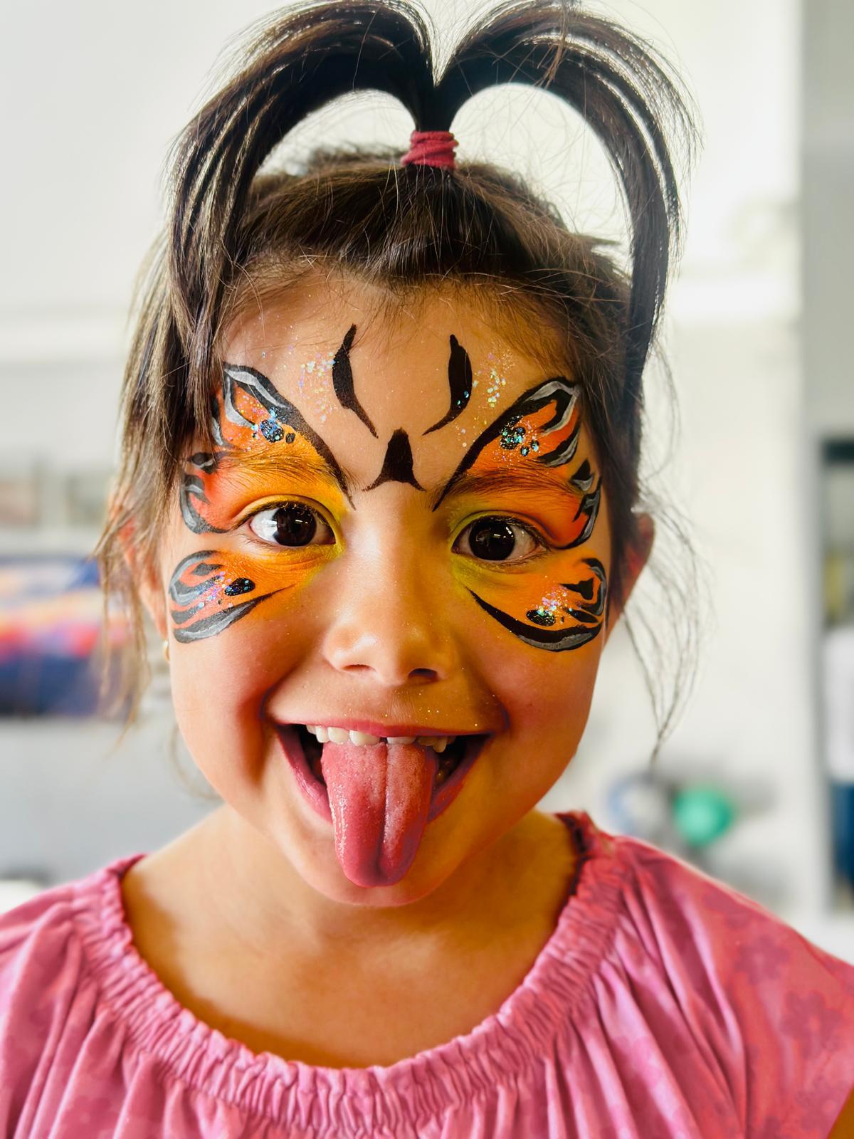 A playful girl with an orange and black butterfly face painting