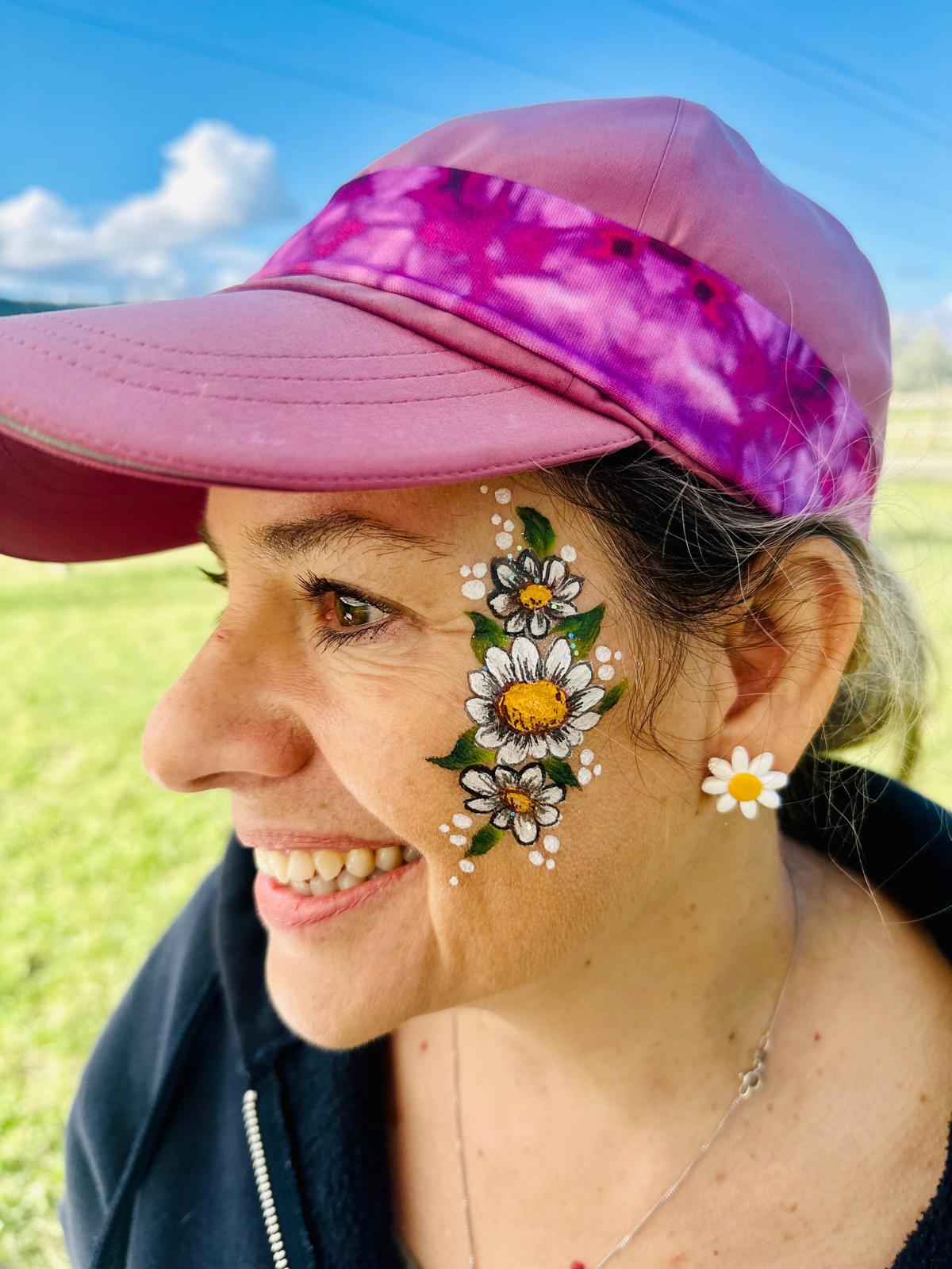 A woman with a detailed white daisy floral face painting on her cheek