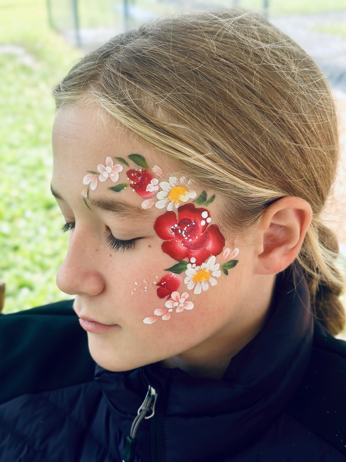 A teenage girl with a floral face painting featuring red roses and white daisies