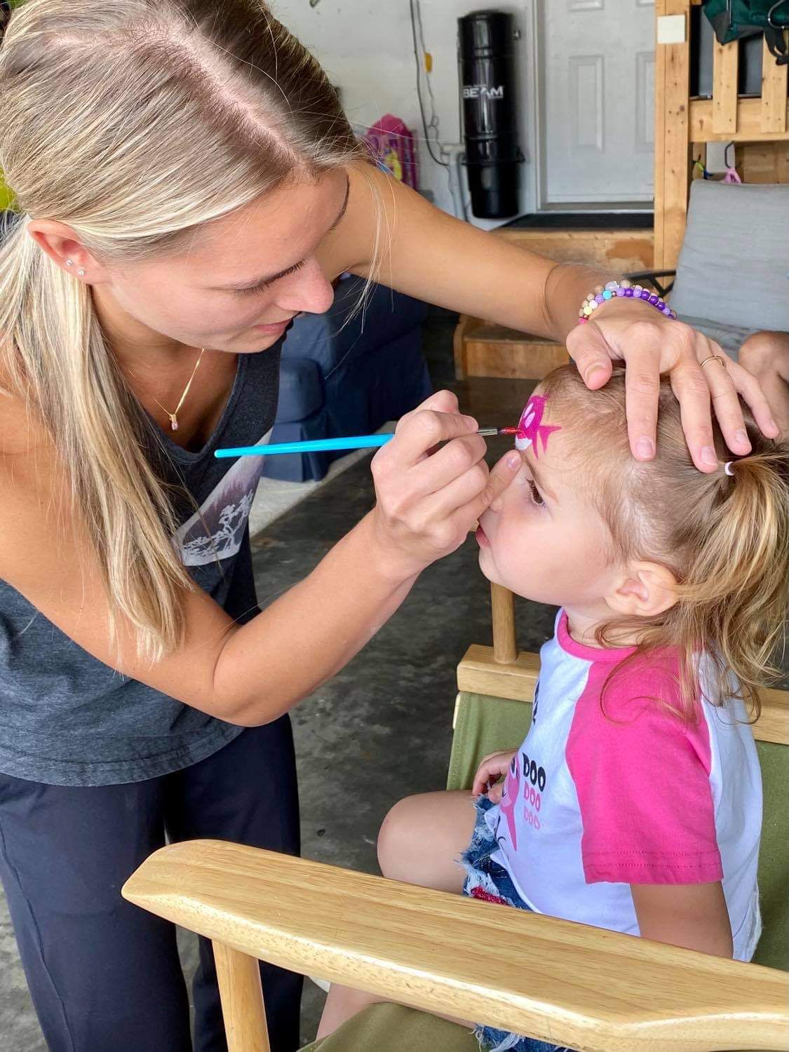 Sofya carefully creating a pink butterfly design on a young girl's face